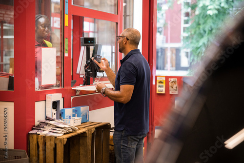 Mature man paying through mobile payment while standing at checkout counter in hardware store photo