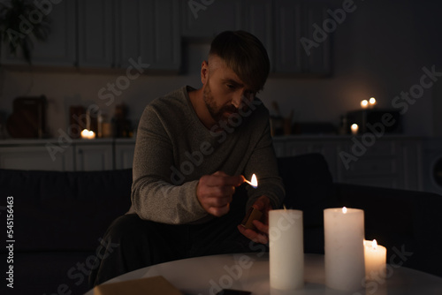 man holding burning match while lighting candles in dark kitchen during power outage.