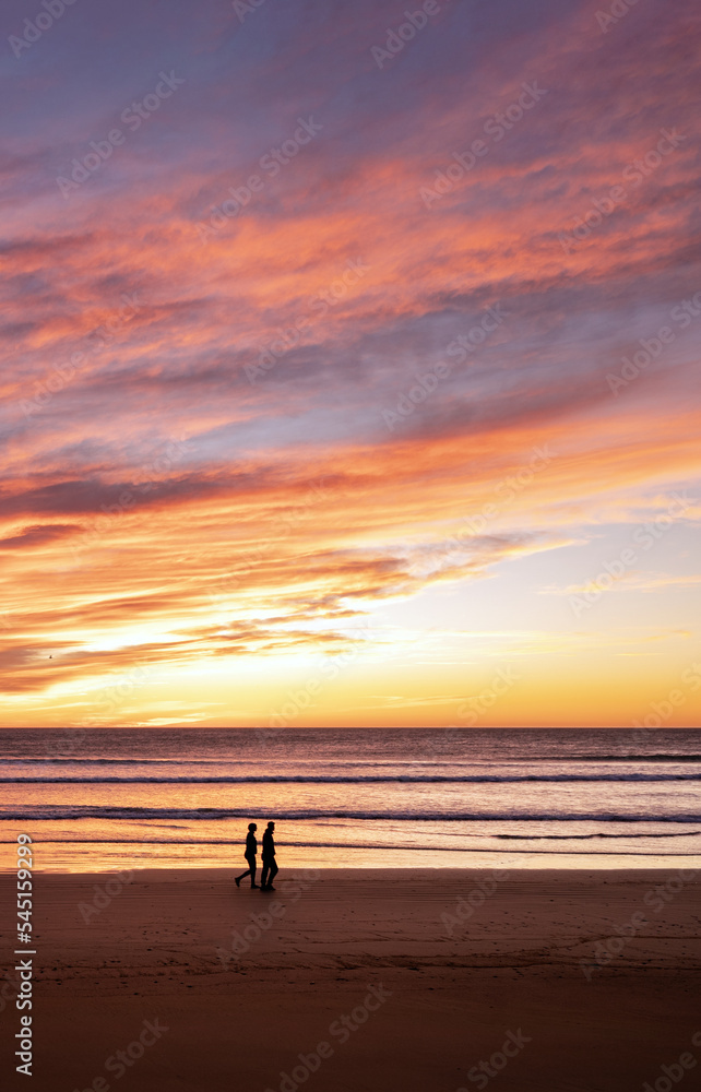 Couple walking along the beach at dramatic sunrise.