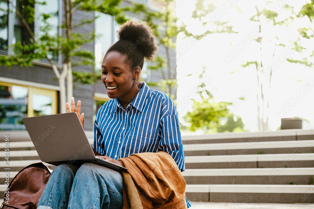 Fototapeta premium Young beautiful smiling african woman holding video conference with laptop