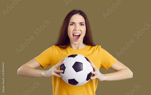 Emotional millennial girl isolated on green studio background hold ball scream support sports team. Excited young Caucasian woman shout cheering football players. Entertainment and hobby concept. © Studio Romantic