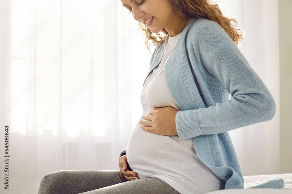 Crop of smiling healthy Caucasian pregnant woman sit on sofa relax on maternity leave at home. Happy young female excited with pregnancy wait for childbirth. Motherhood and parenting.