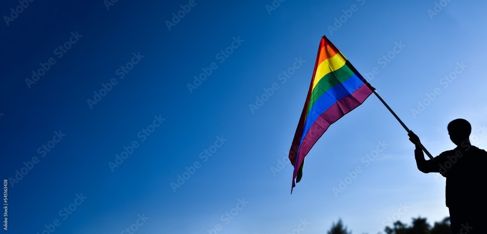Rainbow flag, LGBT simbol, holding in hands of boy against clear bluesky background, soft and selective focus, concept for LGBT celebration in pride month, June, around the world, copy space. Rainbow flag, LGBT simbol, holding in hands of boy against clear bluesky background, soft and selective focus, concept for LGBT celebration in pride month, June, around the world, copy space.