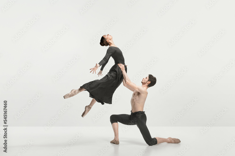 Young man and woman, ballet dancers performing on stage isolated over grey studio background. Support