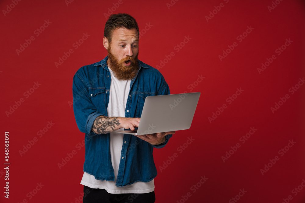 Ginger shocked man wearing denim shirt using laptop