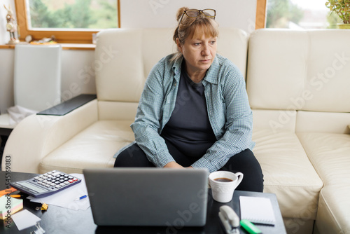 Active mature woman using a laptop for remote work from the home office. Video conference, video meeting. Senior teacher leads webinar