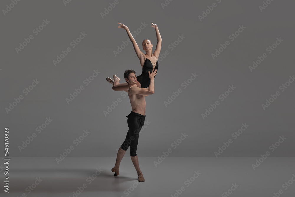 Young man and woman, ballet dancers performing isolated over dark grey studio background. Keeping balance on shoulder Young man and woman, ballet dancers performing isolated over dark grey studio background. Keeping balance on shoulder