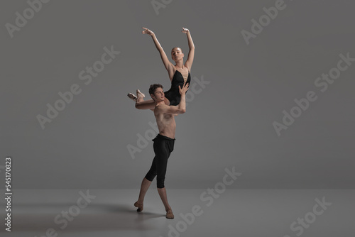 Young man and woman, ballet dancers performing isolated over dark grey studio background. Keeping balance on shoulder