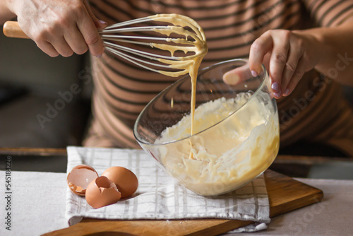 Fotografie Senior woman beats eggs with flour for dough with a wisk in a glass bowl