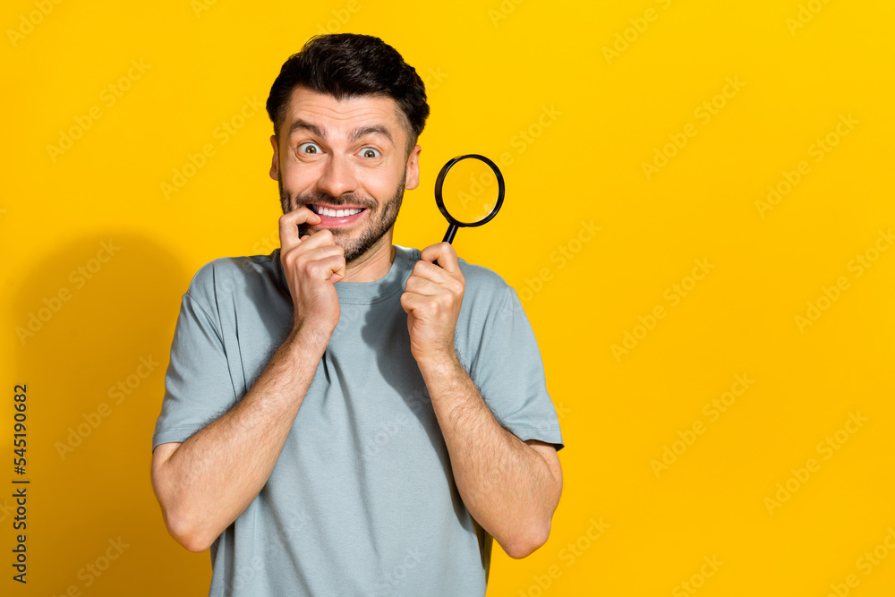 Photo of astonished positive man hold enlarge magnifier teeth bite fingernail empty space wait sale isolated on yellow color background Photo of astonished positive man hold enlarge magnifier teeth bite fingernail empty space wait sale isolated on yellow color background