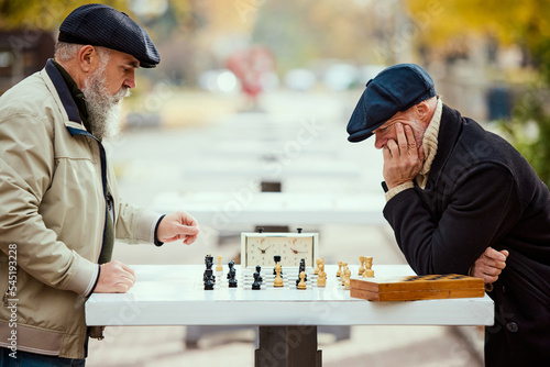 Portrait of two senior men playing chess in the park on a daytime in fall. Thoughtful activity. Concept of leisure activity, old generation