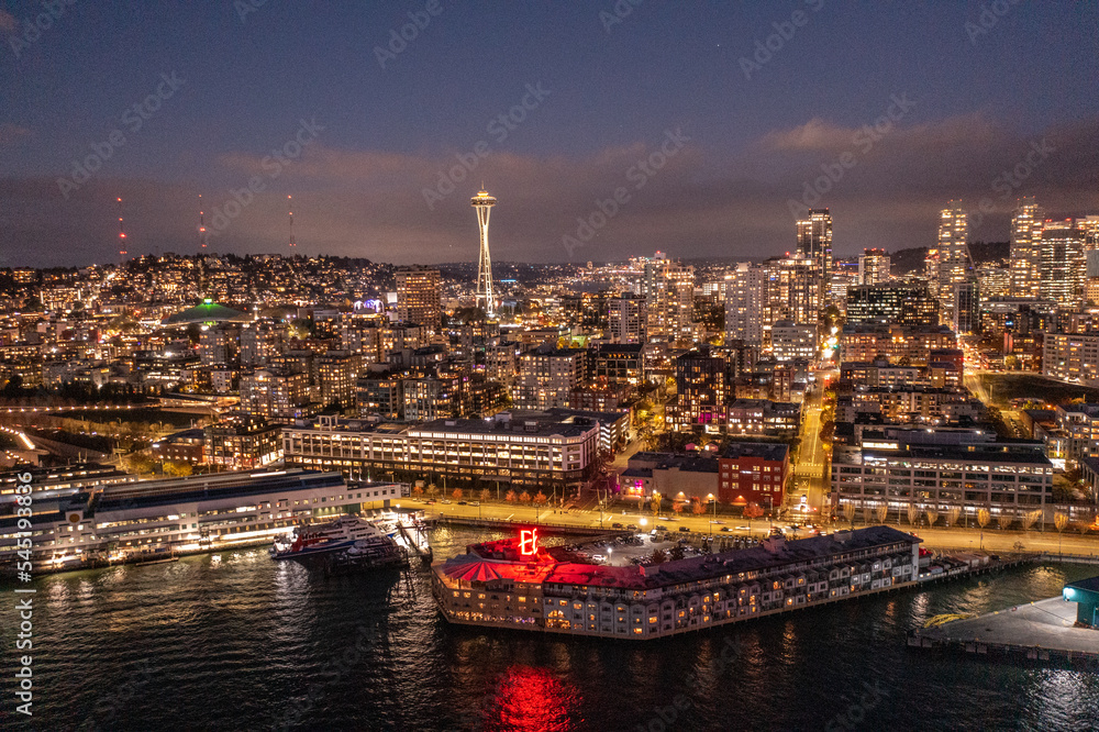 Naklejka premium Seattle, Washington, USA - November 2022, night aerial view of illuminated Seattle Downtown and the Waterfront pier area with famous Space Needle Tower - aerial night view 