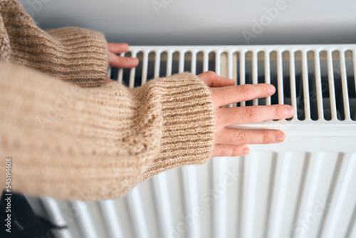 Using heater at home in winter. Young girl warming her hands. Heating season, cold room, heating problems