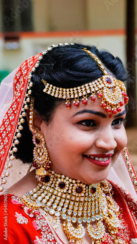 Portrait of a beautiful Indian bride in a traditional wedding dress. Young Hindu woman with golden Kundan jewelry set. Traditional Indian costume lehenga choli.  kalira and red nail paint photo