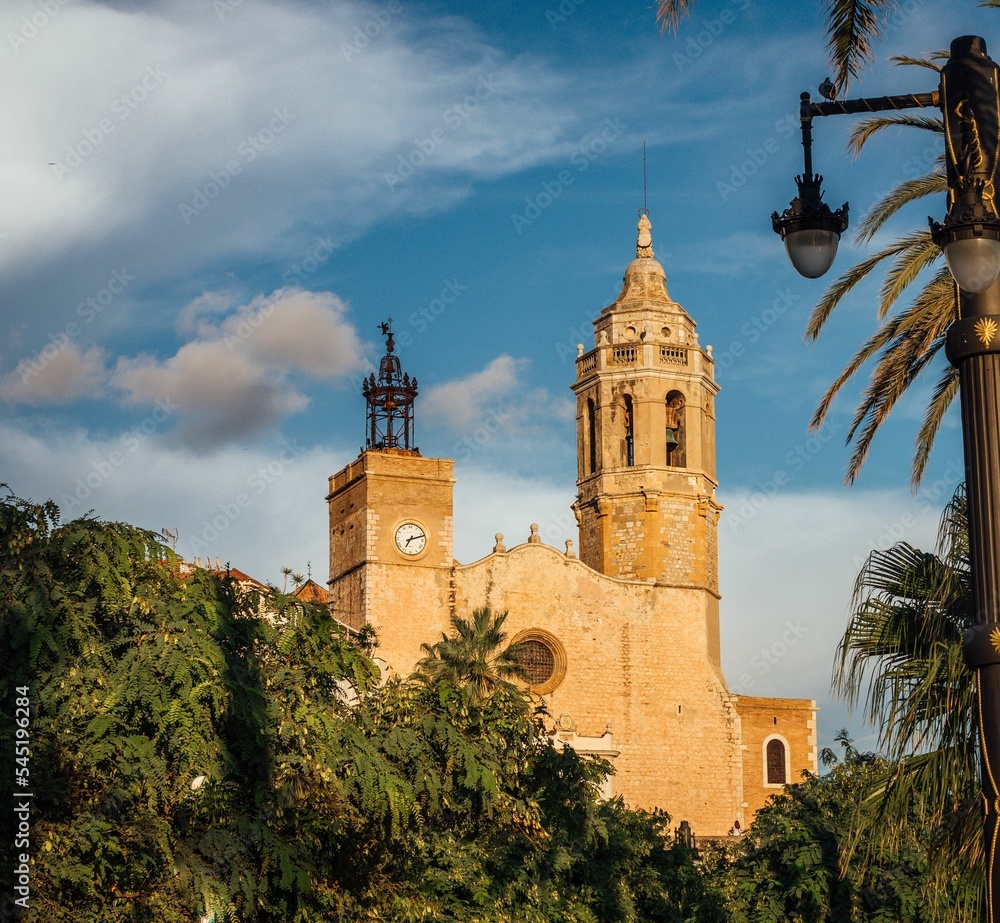 Low angle of a catholic church near the garden, under a blue sky during the daytime in Sitges, Spain