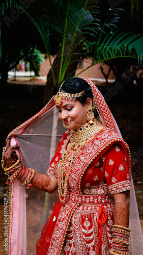 Portrait of a beautiful Indian bride in a traditional wedding dress. Young Hindu woman with golden Kundan jewelry set. Traditional Indian costume lehenga choli.  kalira and red nail paint photo