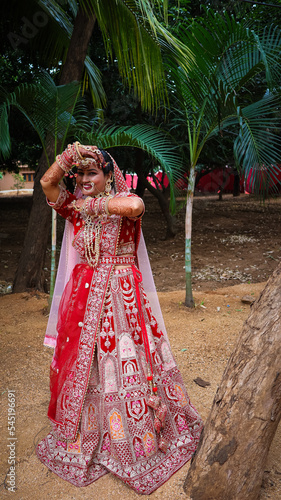 Portrait of a beautiful Indian bride in a traditional wedding dress. Young Hindu woman with golden Kundan jewelry set. Traditional Indian costume lehenga choli.  kalira and red nail paint photo