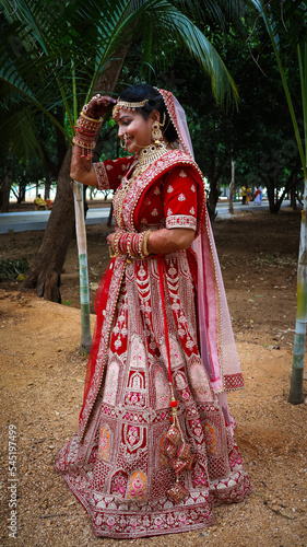 Portrait of a beautiful Indian bride in a traditional wedding dress. Young Hindu woman with golden Kundan jewelry set. Traditional Indian costume lehenga choli.  kalira and red nail paint photo