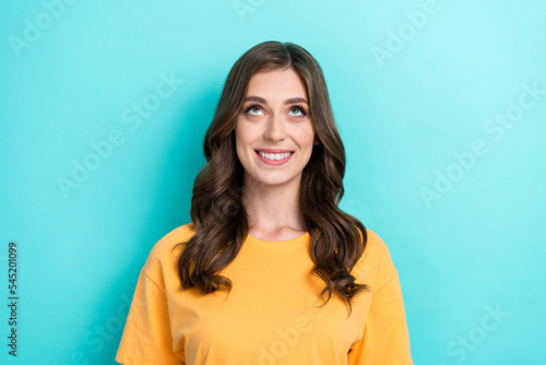 Photo of cute nice pleasant girl with wavy hairstyle wear yellow t-shirt curious look empty space isolated on turquoise color background