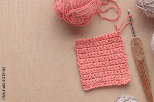 Crochet handmade square pattern, pink yarn coil, hook, knitting crocheting top view on a wooden background