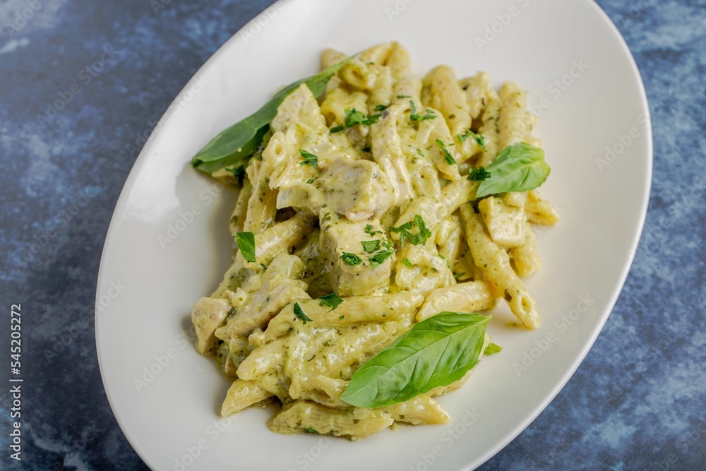 Top view of penne pasta with white sauce decorated with basil leaves on a white plate