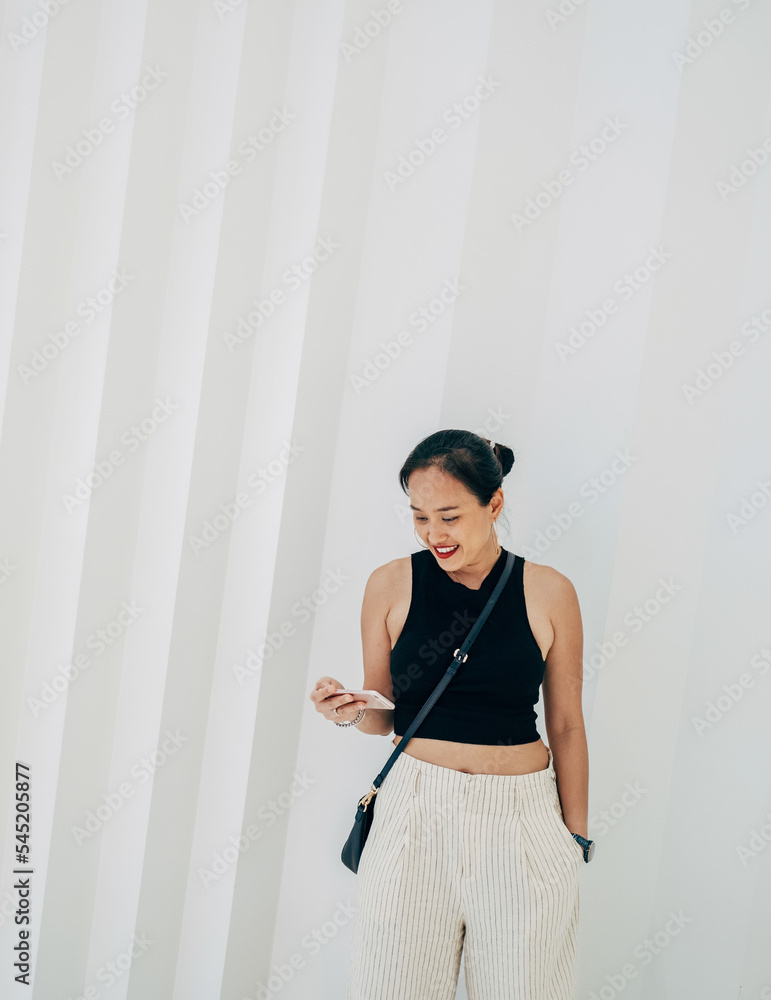 Happy woman watching or reading something on a mobile phone while standing in front of white geometric wall