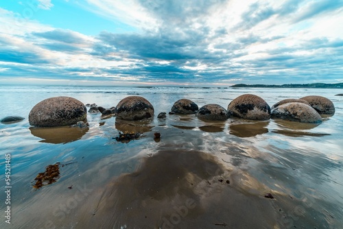 Panoramic view of Moeraki Boulders Beach in Hampden, New Zealand on a cloudy sky photo