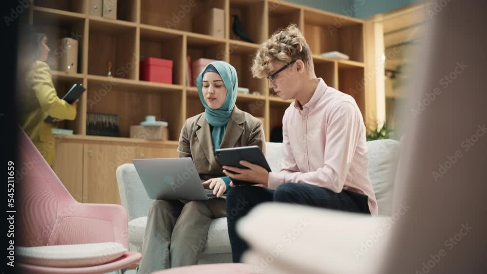 Two Creative Colleagues Collaborating Over a Work Project Using Computer and Tablet at Office. Male E-commerce Marketing Manager Discussing with Muslim Female Media Planner. Medium Slow Motion Shot Two Creative Colleagues Collaborating Over a Work Project Using Computer and Tablet at Office. Male E-commerce Marketing Manager Discussing with Muslim Female Media Planner. Medium Slow Motion Shot