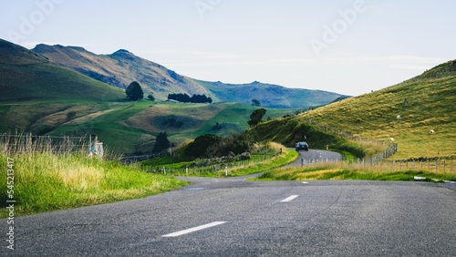 Car driving on a highway road in front of green meadows and mountains, Banks Peninsula, New Zealand