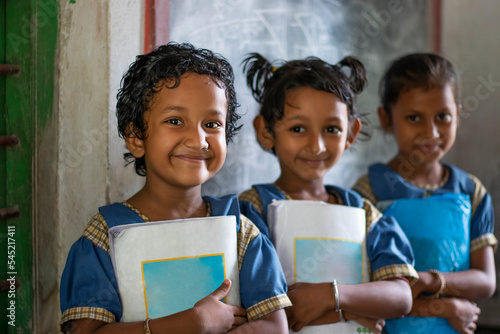 Three School Children's holding books standing at school