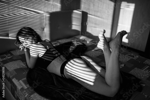 Gorgeous slim woman lies on the bed and relaxes under sun rays. Black and white snapshot of an attractive lady. photo