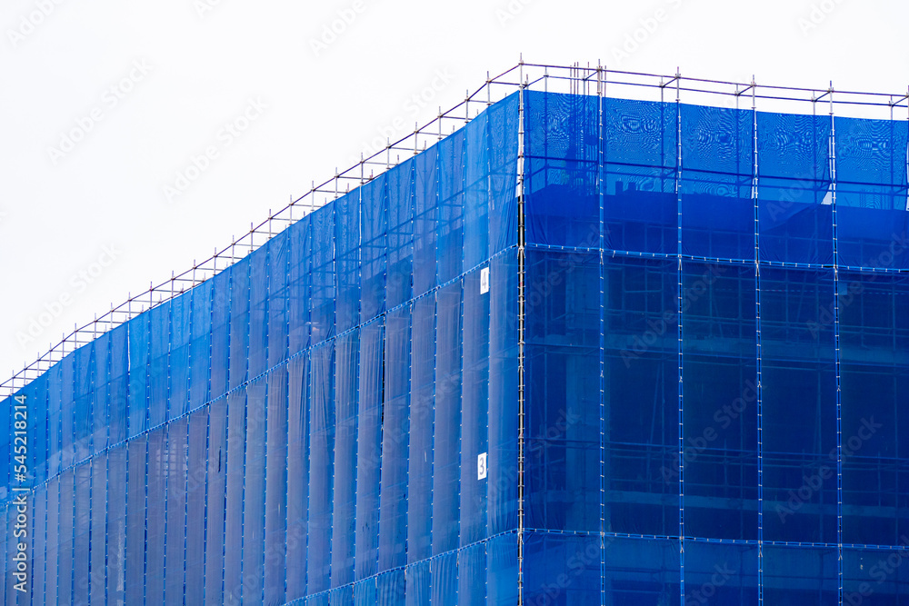 A blue slan surrounds the building under construction.