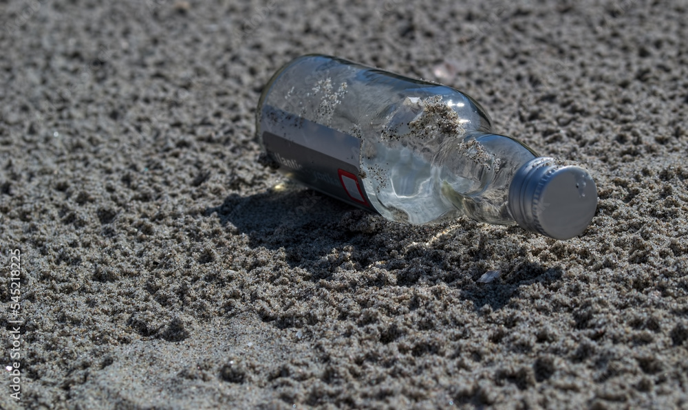 A glass bottle on the sand. Discarded glass bottle lying on sandy beach. A glass bottle on the sand. Discarded glass bottle lying on sandy beach.