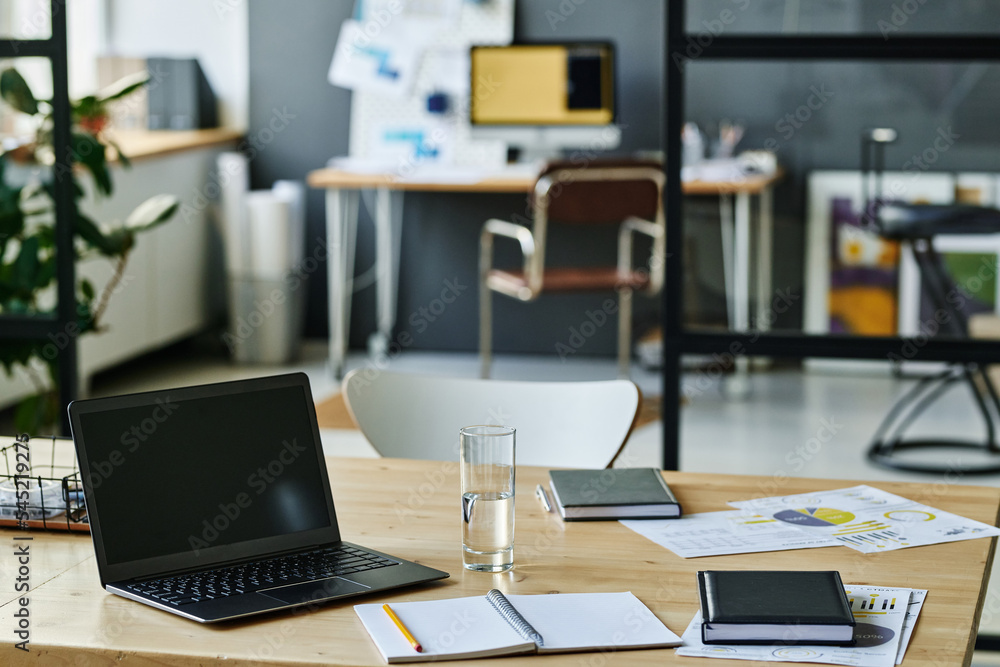 Workplace of economist or accountant with laptop, notebook with pen, glass of water and financial documents in openspace office Workplace of economist or accountant with laptop, notebook with pen, glass of water and financial documents in openspace office