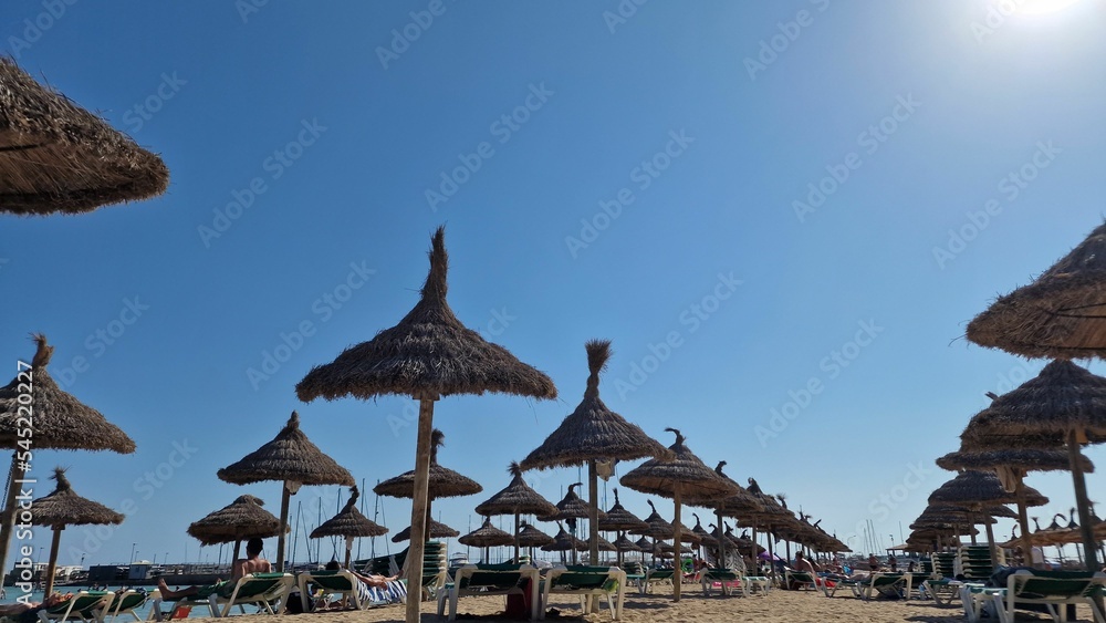Row of thatch parasols and people vacationing on the beach under clear blue sky