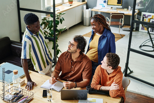 Group of four intercultural managers or creative designers having discussion of their ideas and working strategies at meeting