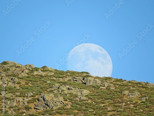 Mountain top and moon against a blue sky in Navacepedilla de Corneja, Avila, Spain