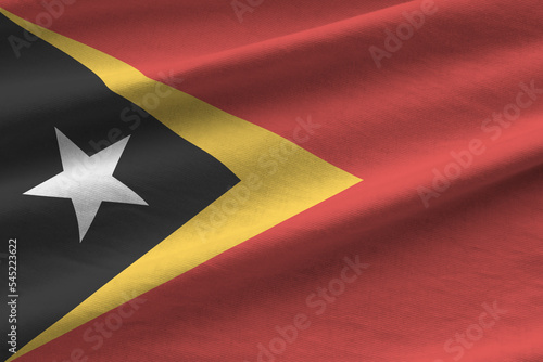 Timor Leste flag with big folds waving close up under the studio light indoors. The official symbols and colors in banner photo