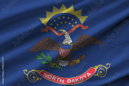 North Dakota US state flag with big folds waving close up under the studio light indoors. The official symbols and colors in banner photo