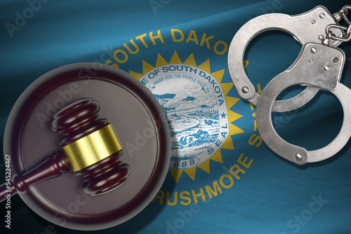 South Dakota US state flag with judge mallet and handcuffs in dark room. Concept of criminal and punishment photo