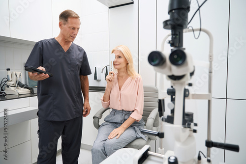 Ophthalmologist standing near the patient and checking vision quality