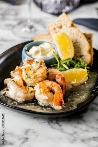 Vertical shot of a shrimp dish with sauce and served with lemon, bread, herbs on a marble background