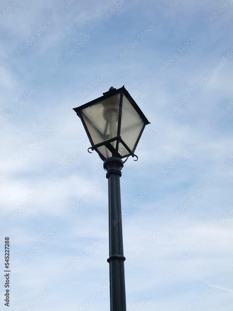 Vertical shot of an old street light on blue cloudy sky background
