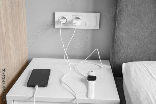devices on charge in the bedroom, smart watch, phone on charge on the bedside table photo