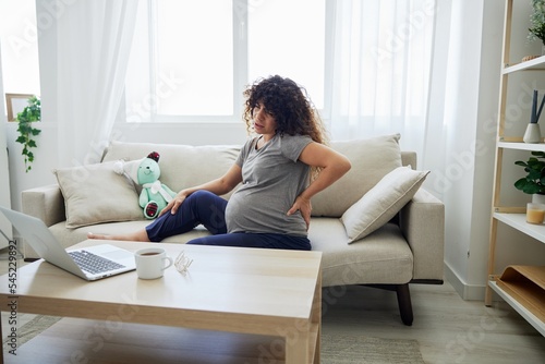 A pregnant woman sits on a sofa with a baby toy rabbit and watches a movie and video chat in a laptop. Lifestyle preparation for childbirth, last month of pregnancy