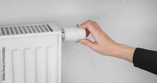 A woman turns the regulator of the thermostatic radiator valve to the middle position to set the economical heating mode of the room. Heating of the apartment in the cold season.