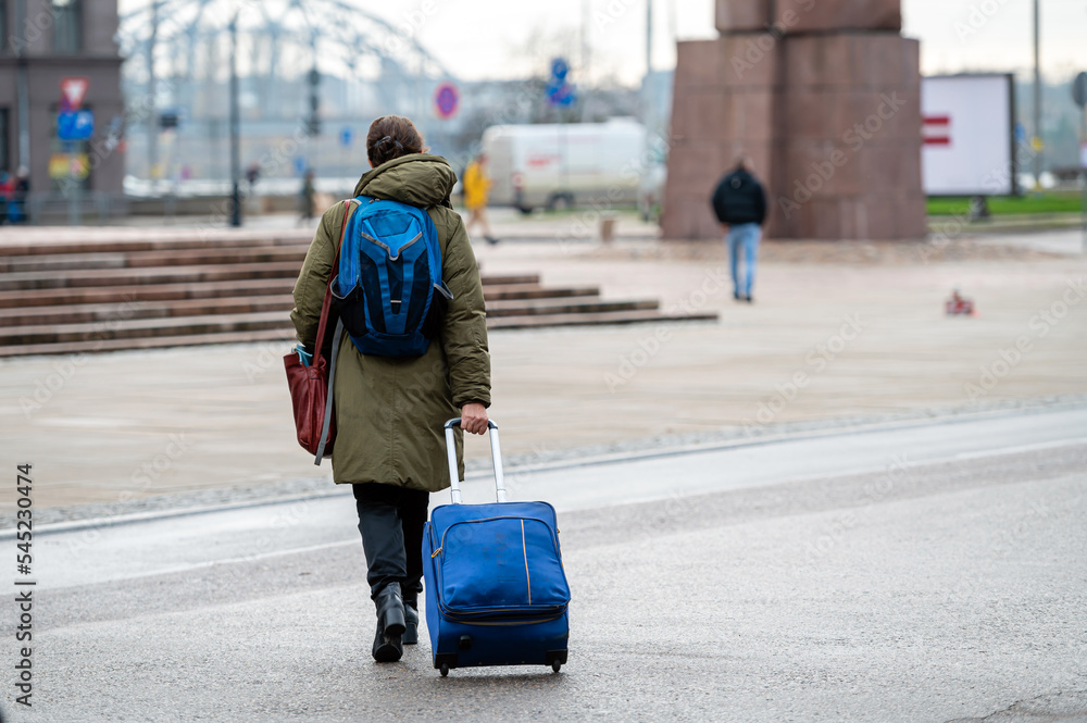 A tourist with a backpack pulls a suitcase on wheels down the street, rear view A tourist with a backpack pulls a suitcase on wheels down the street, rear view