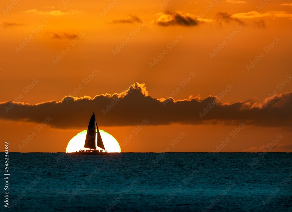 Silhouette of a sailboat in the ocean against the golden sunset sky under a golden sky