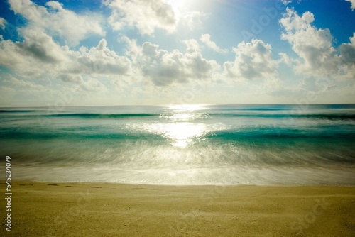 Blue ocean with a sandy beach and sunlight reflected in the waters under blue sky