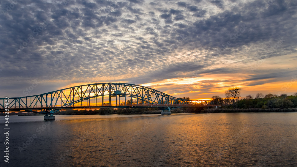 Naklejka premium Zachód słońca, nad rzeką w tle most.